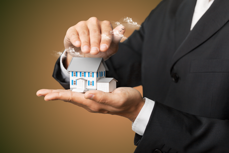 Zwei Hände eines Mannes im Anzug halten ein kleines Modellhaus mit Rauch aus dem Schornstein Zwei Hände eines Mannes im Anzug halten ein kleines Modellhaus mit Rauch aus dem Schornstein