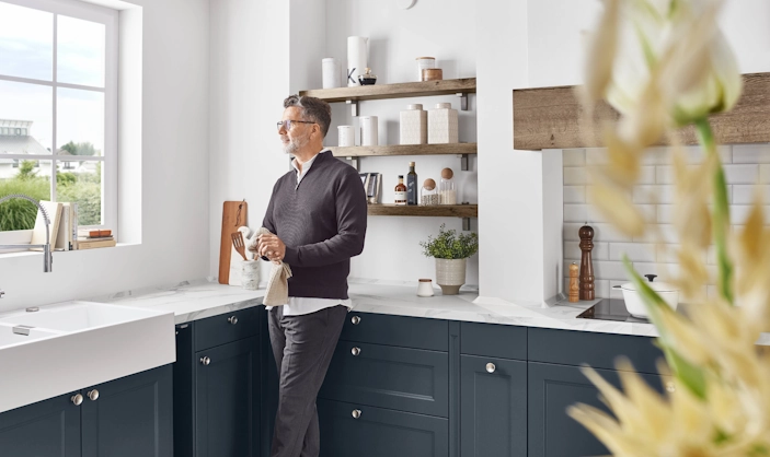 Mann steht in einer Küche und sieht aus dem Fenster, während er sich seine Hände abtrocknet. Mann steht in einer Küche und sieht aus dem Fenster, während er sich seine Hände abtrocknet.