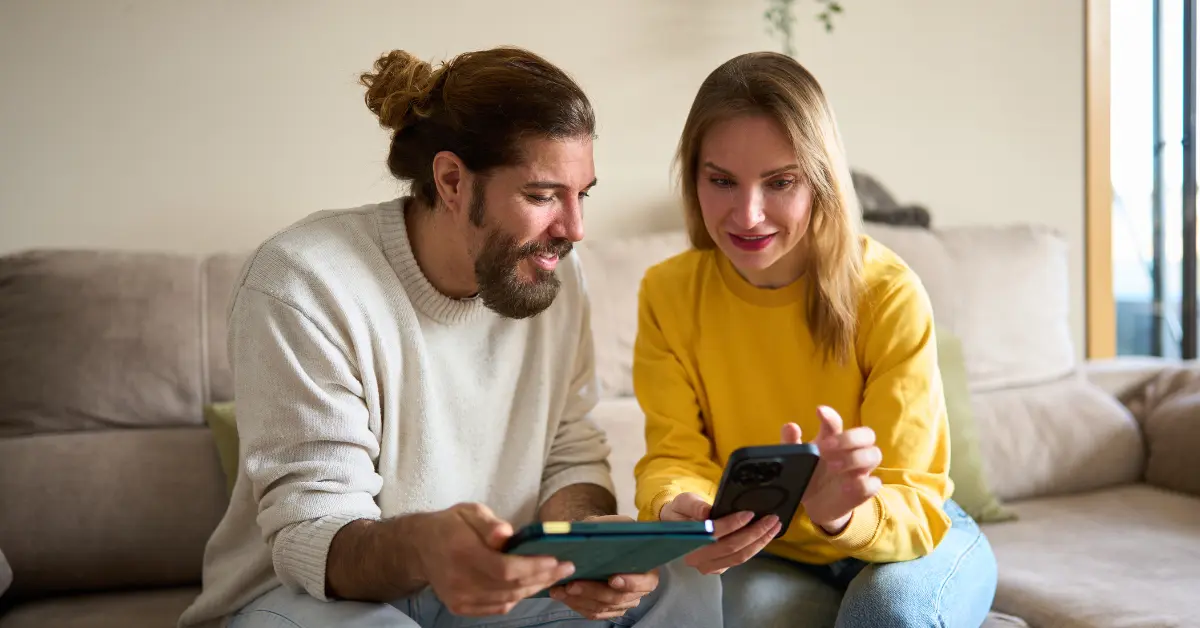 Zwei Personen sitzen auf einem Sofa und schauen gemeinsam auf ein Smartphone und ein Tablet Zwei Personen sitzen auf einem Sofa und schauen gemeinsam auf ein Smartphone und ein Tablet