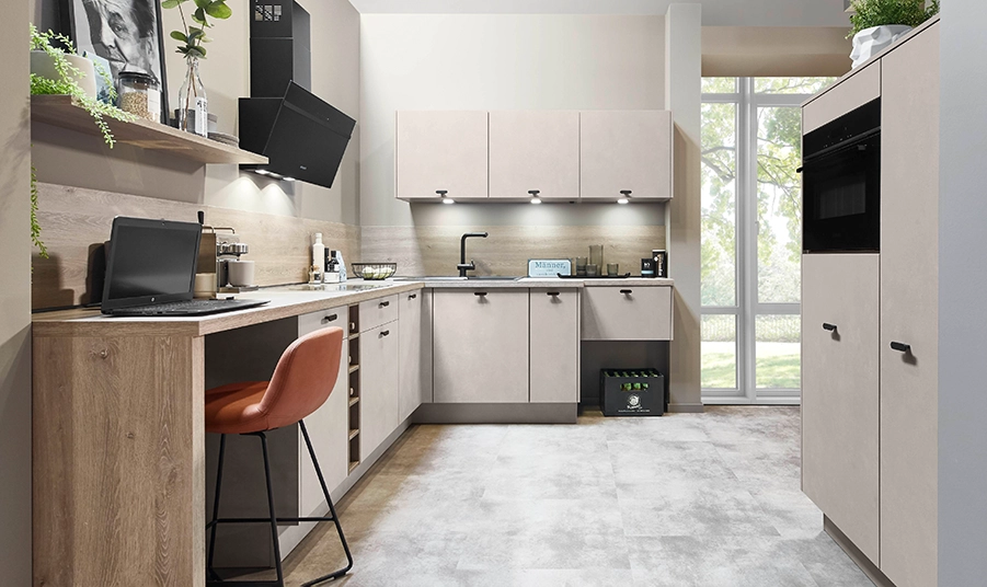 Blick in eine beige Eckküche mit Highboards und kleiner Theke. Auf der Theke steht ein Laptop. Blick in eine beige Eckküche mit Highboards und kleiner Theke. Auf der Theke steht ein Laptop.