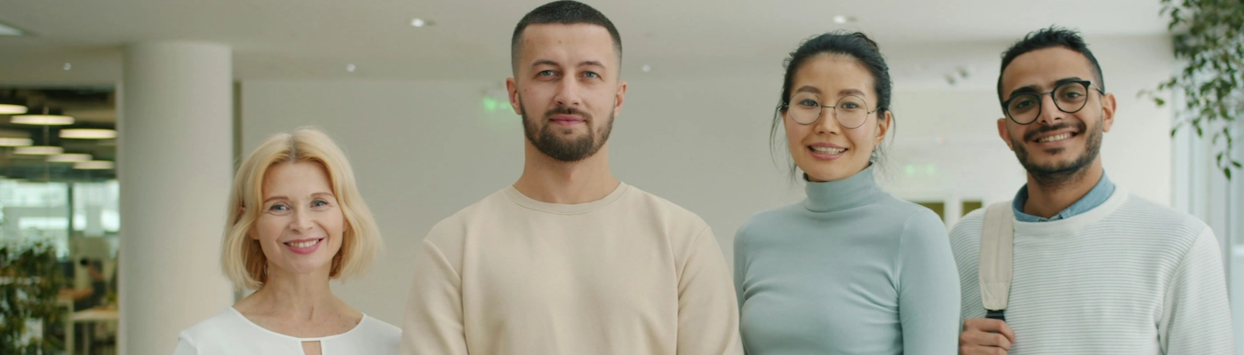 Vier Personen stehen nebeneinander in einem modernen Bürogebäude und lächeln freundlich in die Kamera. Vier Personen stehen nebeneinander in einem modernen Bürogebäude und lächeln freundlich in die Kamera.