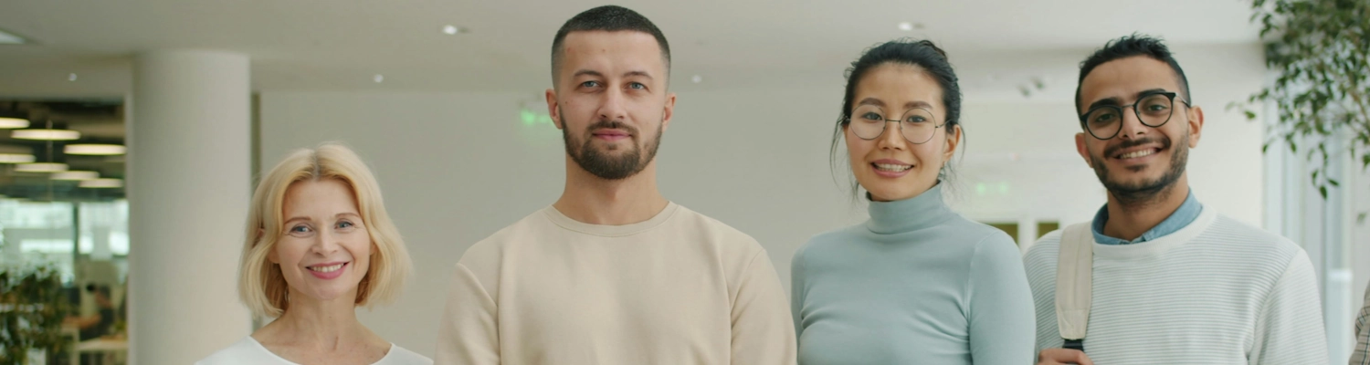 Vier Personen stehen nebeneinander in einem modernen Bürogebäude und lächeln freundlich in die Kamera. Vier Personen stehen nebeneinander in einem modernen Bürogebäude und lächeln freundlich in die Kamera.
