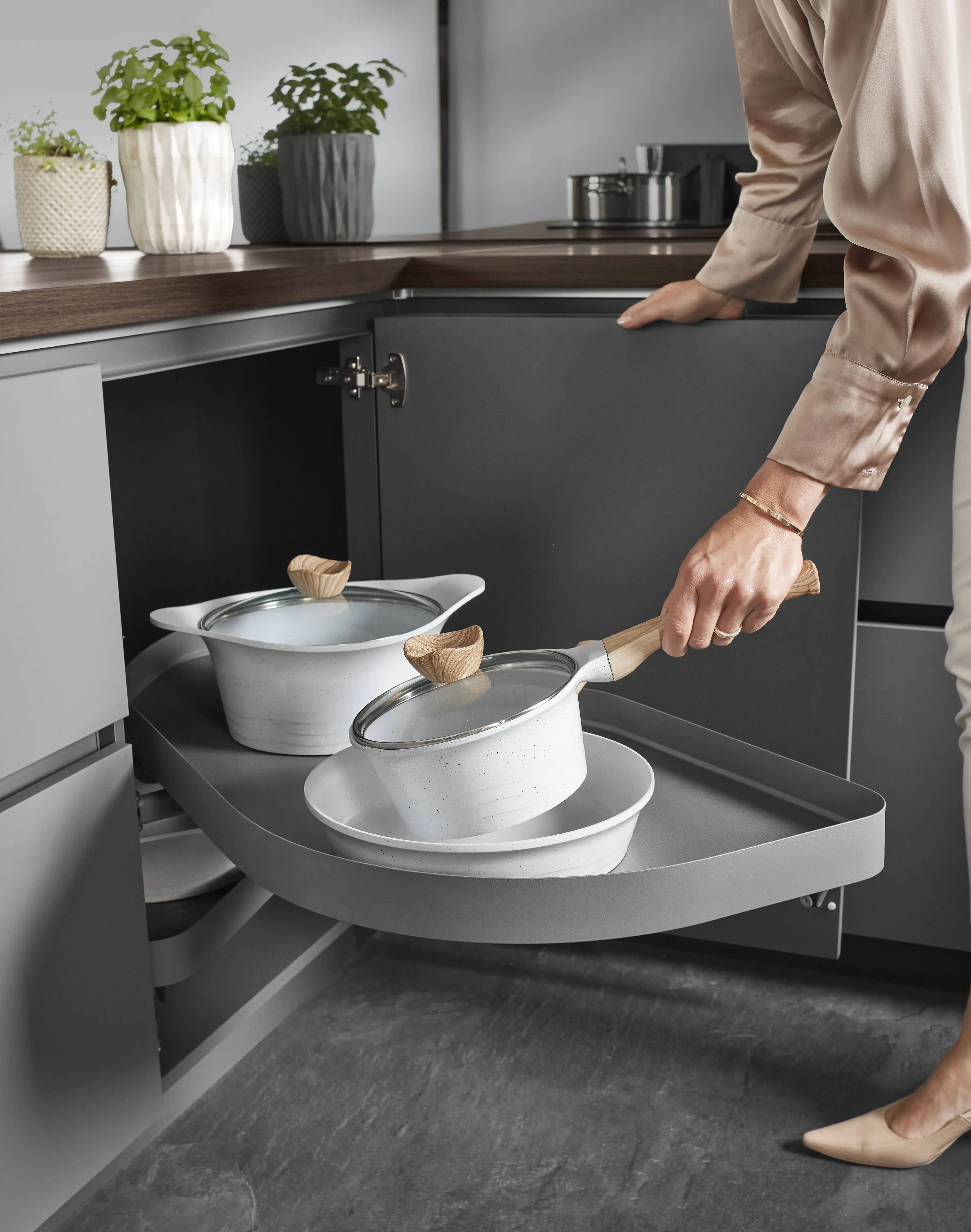 Frau legt Topf in den Eckschrank einer grauen Küche