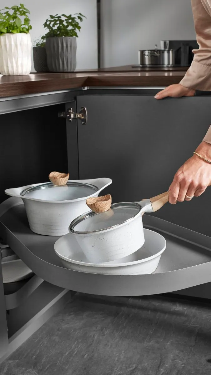 Frau legt Topf in den Eckschrank einer grauen Küche Frau legt Topf in den Eckschrank einer grauen Küche