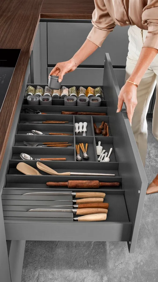 Eine Hand greift zu einem Gewürzbehälter in einer tiefen und gut organisierten anthrazitfarbenen Küchenschublade für Besteck und Kochutensilien. Eine Hand greift zu einem Gewürzbehälter in einer tiefen und gut organisierten anthrazitfarbenen Küchenschublade für Besteck und Kochutensilien.