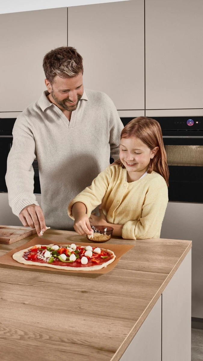 Vater und Tochter belegen zusammen eine Pizza in einer Küche Vater und Tochter belegen zusammen eine Pizza in einer Küche