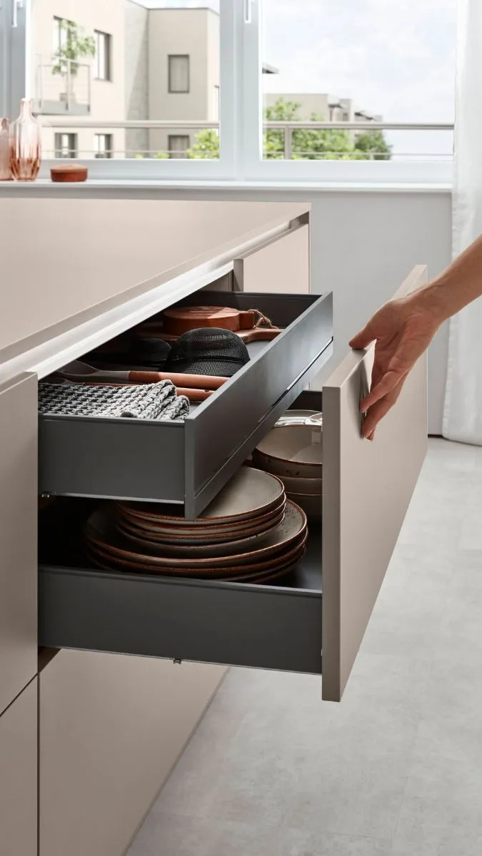 Eine Hand öffnet zwei ausziehbare, tiefe Schubladen in einer hellen Küche, in denen Geschirr und Küchenutensilien ordentlich aufbewahrt werden. Eine Hand öffnet zwei ausziehbare, tiefe Schubladen in einer hellen Küche, in denen Geschirr und Küchenutensilien ordentlich aufbewahrt werden.