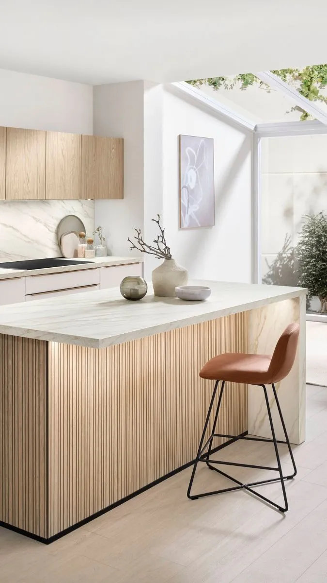 Moderne Küche mit hellen Holzfronten, Marmor-Arbeitsplatte und einer Kücheninsel mit geriffelter Holzverkleidung und einem braunen Barhocker Moderne Küche mit hellen Holzfronten, Marmor-Arbeitsplatte und einer Kücheninsel mit geriffelter Holzverkleidung und einem braunen Barhocker