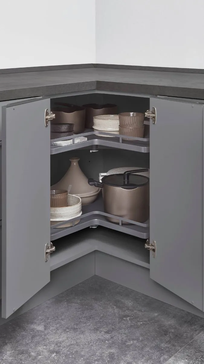Geöffneter grauer Eckschrank mit zwei Drehböden, auf denen Geschirr und Vorratsbehälter gelagert werden. Geöffneter grauer Eckschrank mit zwei Drehböden, auf denen Geschirr und Vorratsbehälter gelagert werden.