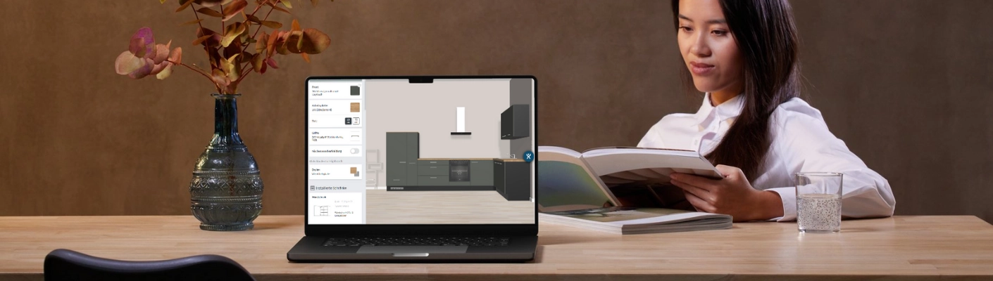 Person sitzt am Tisch und plant eine Küche am Laptop mit einem digitalen Küchenplaner, daneben liegt ein geöffnetes Magazin, auf dem Tisch stehen eine Vase und ein Glas Wasser. Person sitzt am Tisch und plant eine Küche am Laptop mit einem digitalen Küchenplaner, daneben liegt ein geöffnetes Magazin, auf dem Tisch stehen eine Vase und ein Glas Wasser.