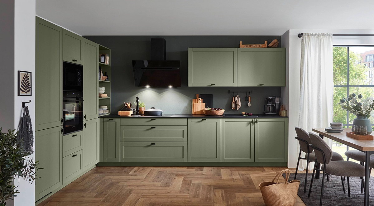 Moderne Küche mit grün-matten Fronten, schwarzer Arbeitsplatte, schwarzem Dunstabzug und offenen Regalen; rechts ein heller Essbereich vor großen Fensterflächen. Moderne Küche mit grün-matten Fronten, schwarzer Arbeitsplatte, schwarzem Dunstabzug und offenen Regalen; rechts ein heller Essbereich vor großen Fensterflächen.