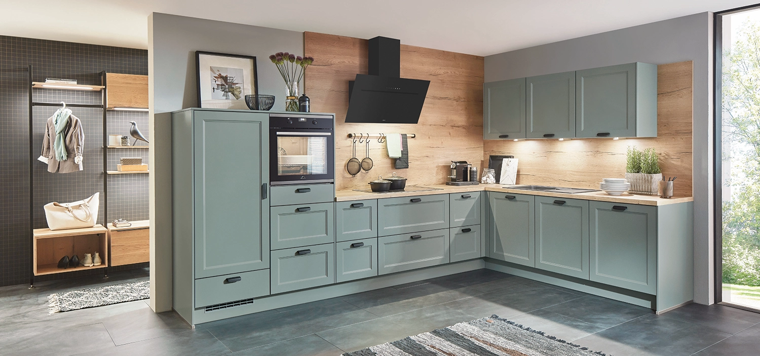 Moderne L-Küche mit mattgrünen Landhausfronten, Holzrückwand, schwarzem Dunstabzug und integriertem Backofen; daneben offener Garderobenbereich mit Holz- und Schwarzakzenten. Moderne L-Küche mit mattgrünen Landhausfronten, Holzrückwand, schwarzem Dunstabzug und integriertem Backofen; daneben offener Garderobenbereich mit Holz- und Schwarzakzenten.