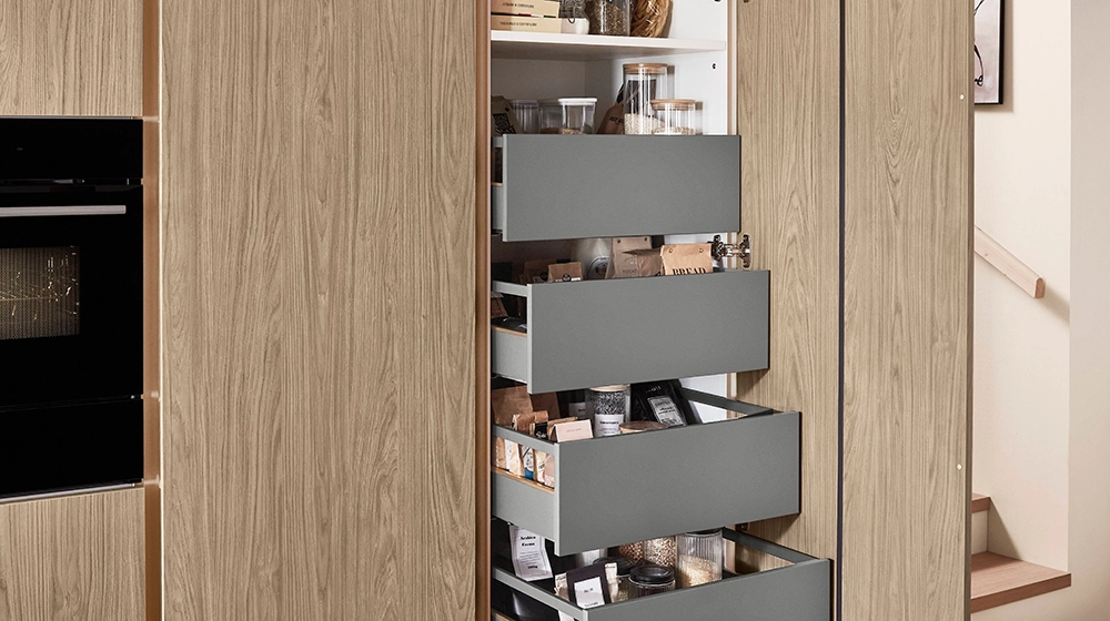 Geöffneter Hochschrank in einer einzeiligen Küche mit Innenschubkästen für viel Stauraum. Die Fronten haben ein Holzdekor. Geöffneter Hochschrank in einer einzeiligen Küche mit Innenschubkästen für viel Stauraum. Die Fronten haben ein Holzdekor.