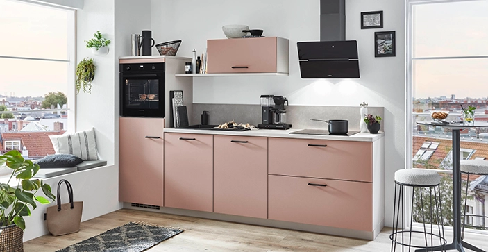 Eine lachsfarbene einzeilige Küche mit Highboard sowie kopffreier Dunsthaube. Die Griffe sind schwarz und die Arbeitsplatte weiß. Eine lachsfarbene einzeilige Küche mit Highboard sowie kopffreier Dunsthaube. Die Griffe sind schwarz und die Arbeitsplatte weiß.