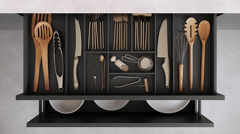 Wir sehen eine geöffnete Küchenschublade mit Besteckeinsatz. Darunter ist ein Auszug geöffnet, in dem Teller aufbewahrt werden. Wir sehen eine geöffnete Küchenschublade mit Besteckeinsatz. Darunter ist ein Auszug geöffnet, in dem Teller aufbewahrt werden.
