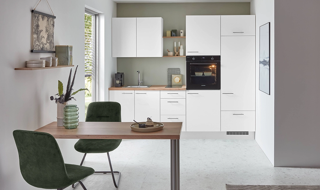 Schmale Küchenzeile mit weißer matter Front und grauem Griff. Die Arbeitsplatte ist in einem Holzton und der Ofen hoch eingebaut. Schmale Küchenzeile mit weißer matter Front und grauem Griff. Die Arbeitsplatte ist in einem Holzton und der Ofen hoch eingebaut.