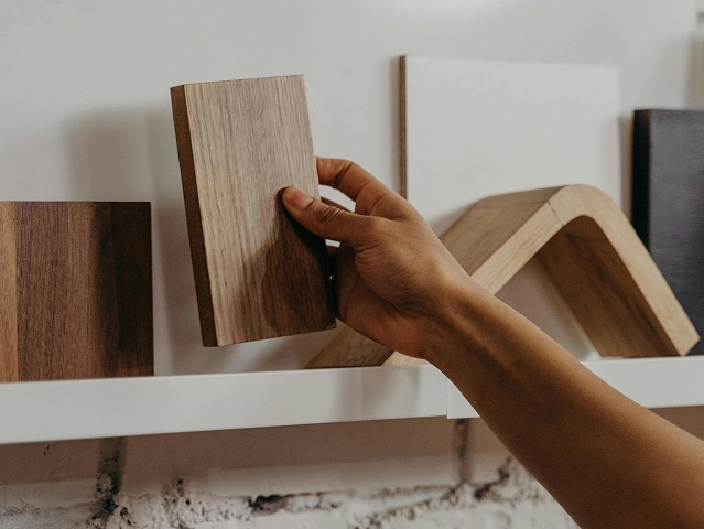 Eine Person hält ein Stück Holz, während sie neben einem mit verschiedenen Gegenständen gefüllten Regal steht. Eine Person hält ein Stück Holz, während sie neben einem mit verschiedenen Gegenständen gefüllten Regal steht.