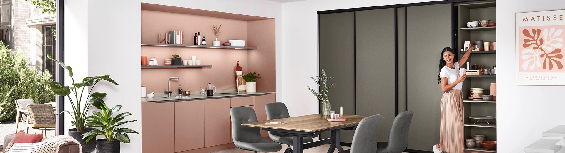 Eine junge Frau mit rose Hose und weißem T-Shirt freut sich über ihren erfolgreichen Frühjahrsputz in der Küche. Die Küchenzeile ist lachsrosa, rechts davon eine graue Schiebetürwand. Eine junge Frau mit rose Hose und weißem T-Shirt freut sich über ihren erfolgreichen Frühjahrsputz in der Küche. Die Küchenzeile ist lachsrosa, rechts davon eine graue Schiebetürwand.