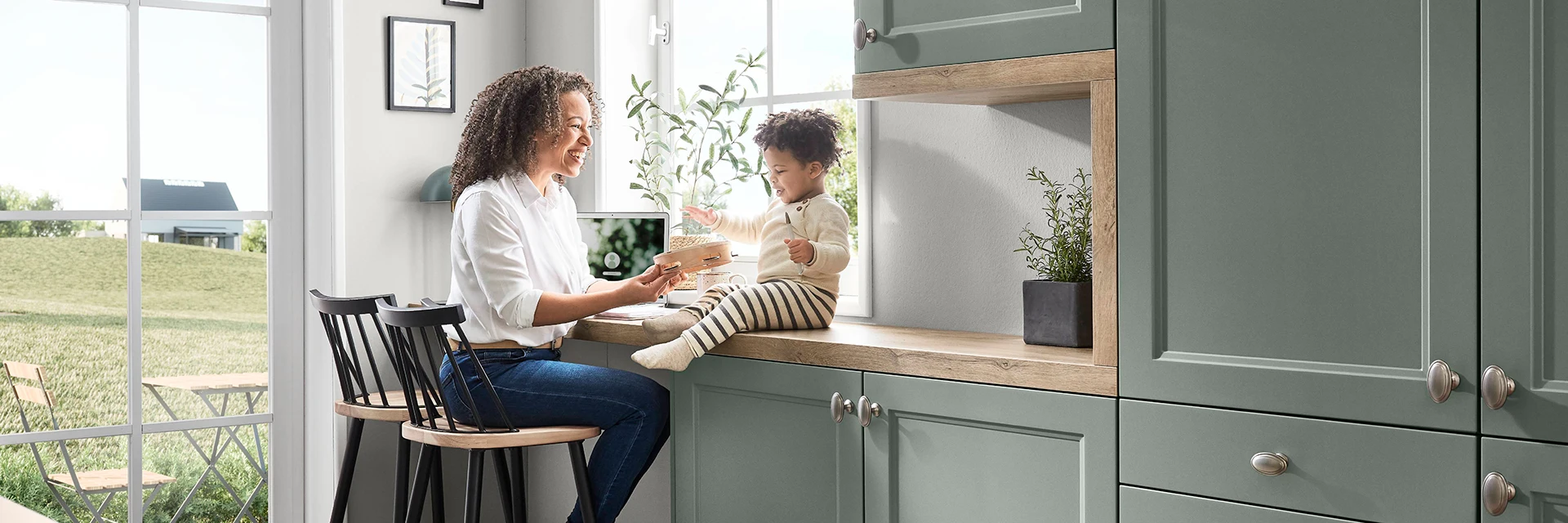 Moderne Küche mit Holzarbeitsplatte, Frau und Kind interagieren neben einem Fenster. Moderne Küche mit Holzarbeitsplatte, Frau und Kind interagieren neben einem Fenster.