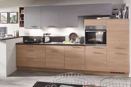 Moderne Einbauküche mit Unterschränken in Holzoptik und grauen Hängeschränken, schwarzer Arbeitsplatte, integriertem Backofen und indirekter Beleuchtung über der Arbeitsfläche. Moderne Einbauküche mit Unterschränken in Holzoptik und grauen Hängeschränken, schwarzer Arbeitsplatte, integriertem Backofen und indirekter Beleuchtung über der Arbeitsfläche.
