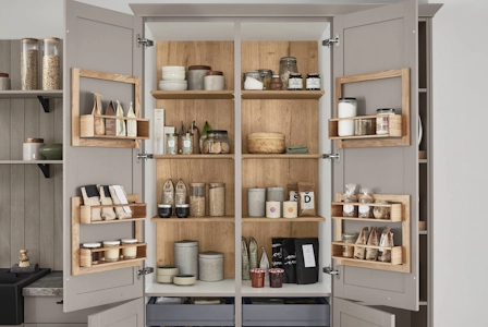 Offener Vorratsschrank mit grauen Türen und Holzinnenraum, übersichtlich gefüllt mit Gläsern, Gewürzen, Dosen und Körben auf Regalböden sowie in Türablagen. Offener Vorratsschrank mit grauen Türen und Holzinnenraum, übersichtlich gefüllt mit Gläsern, Gewürzen, Dosen und Körben auf Regalböden sowie in Türablagen.