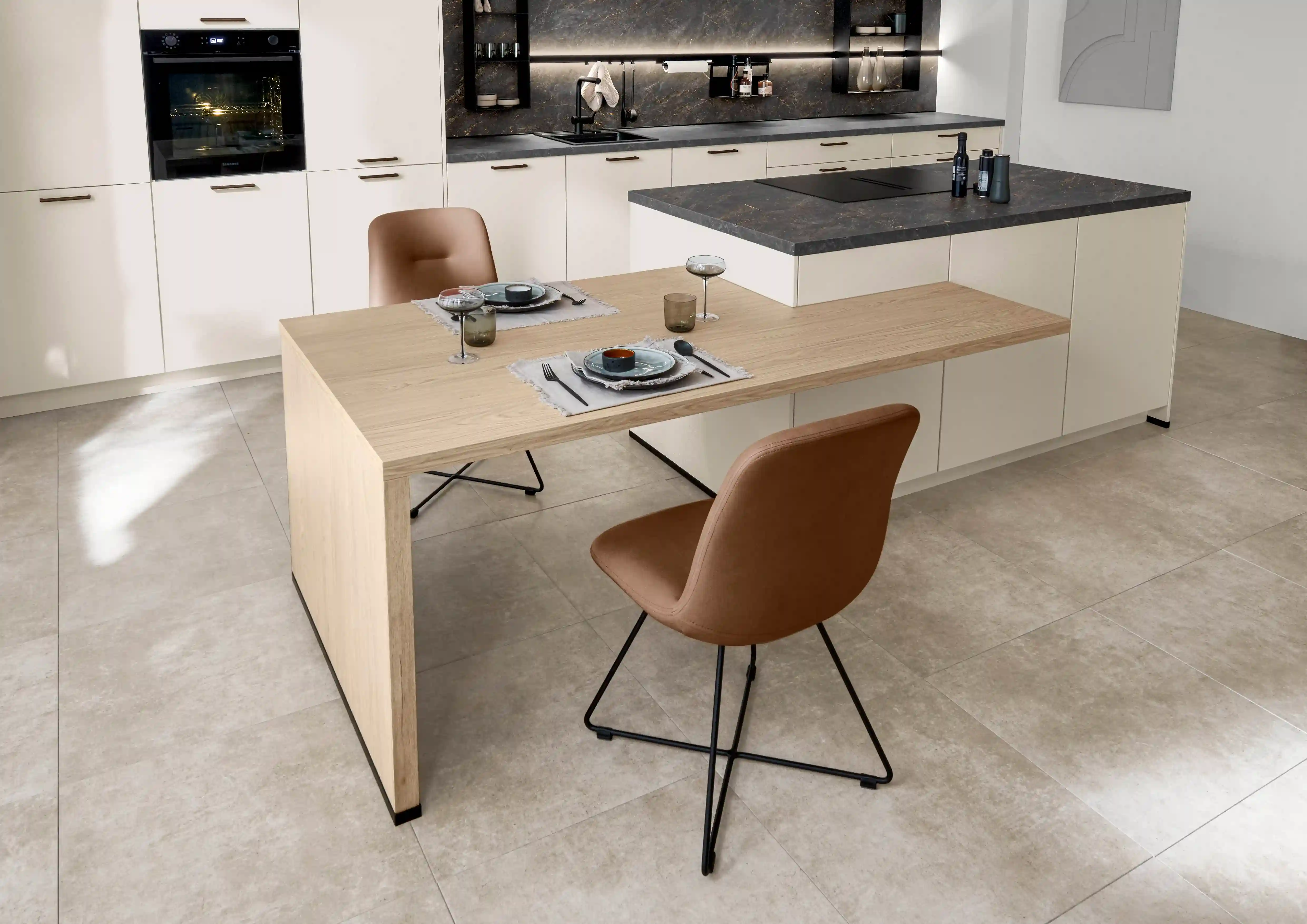 Gedeckter Esstisch an einer cremfarbenen Inselküche mit dunkler Arbeitsplatte im klassischen Küchenstil Gedeckter Esstisch an einer cremfarbenen Inselküche mit dunkler Arbeitsplatte im klassischen Küchenstil