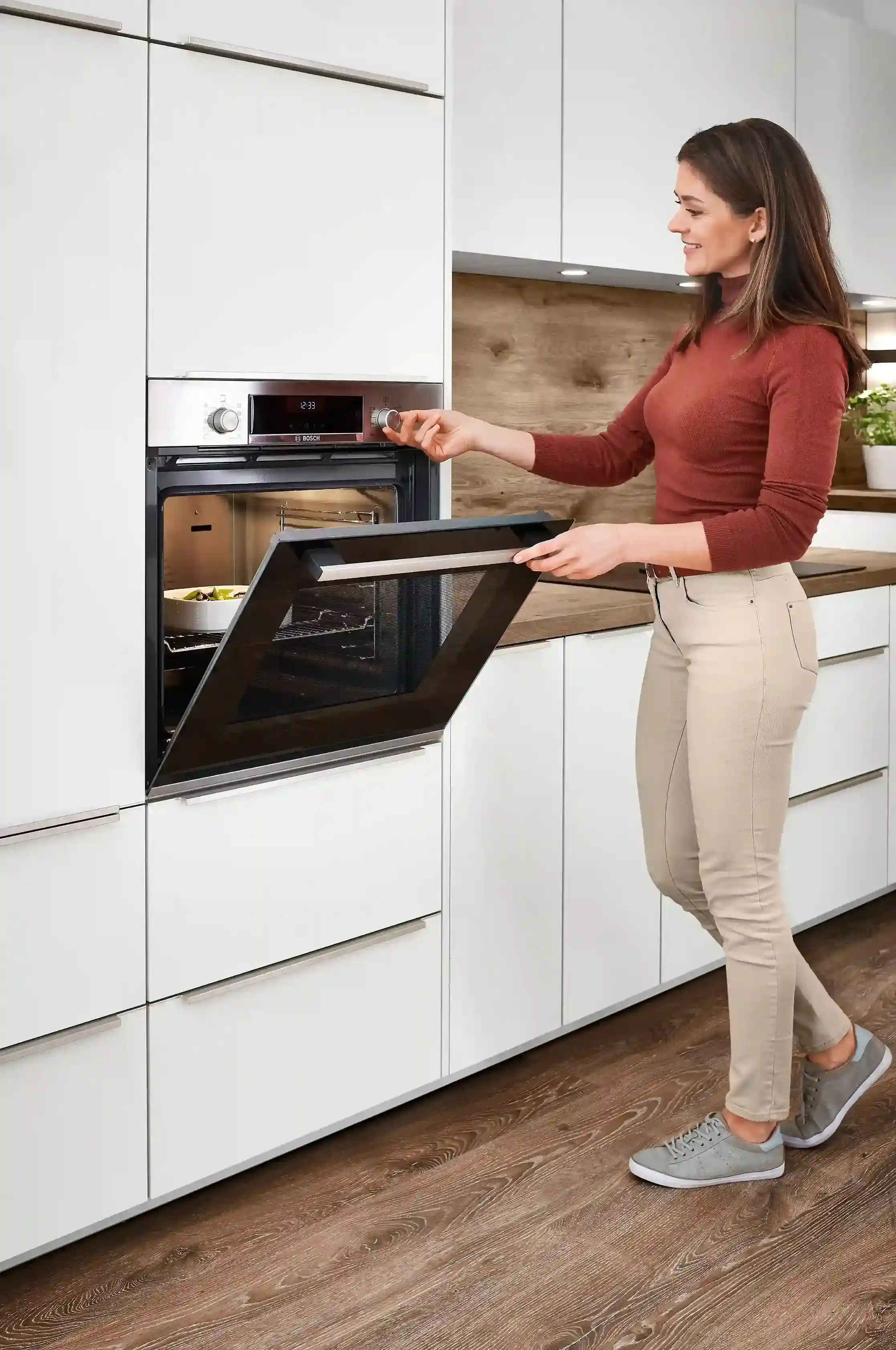 Frau bedient einen Backofen in einer weißen klassischen Küche, in der moderne Technik auf klassisches Design trifft Frau bedient einen Backofen in einer weißen klassischen Küche, in der moderne Technik auf klassisches Design trifft