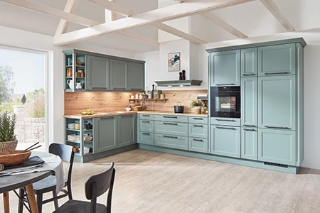 L-Küche im modern Country Stil mit schilfgrünen Rahmenfronten. Die Nischenwandverkleidung und Arbeitsplatte sind in einem Holzton gehalten. Rechts drei Hochschränke, an der linken Ecke offene Regale. L-Küche im modern Country Stil mit schilfgrünen Rahmenfronten. Die Nischenwandverkleidung und Arbeitsplatte sind in einem Holzton gehalten. Rechts drei Hochschränke, an der linken Ecke offene Regale.