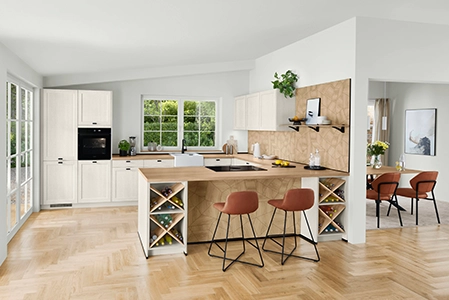 U-Kueche im Landshausstil mit hellen Fronten und Knopfgriffen. Gegenüber der Herdplatte ist eine Theke integriert, vor der zwei Barhocker stehen. U-Kueche im Landshausstil mit hellen Fronten und Knopfgriffen. Gegenüber der Herdplatte ist eine Theke integriert, vor der zwei Barhocker stehen.