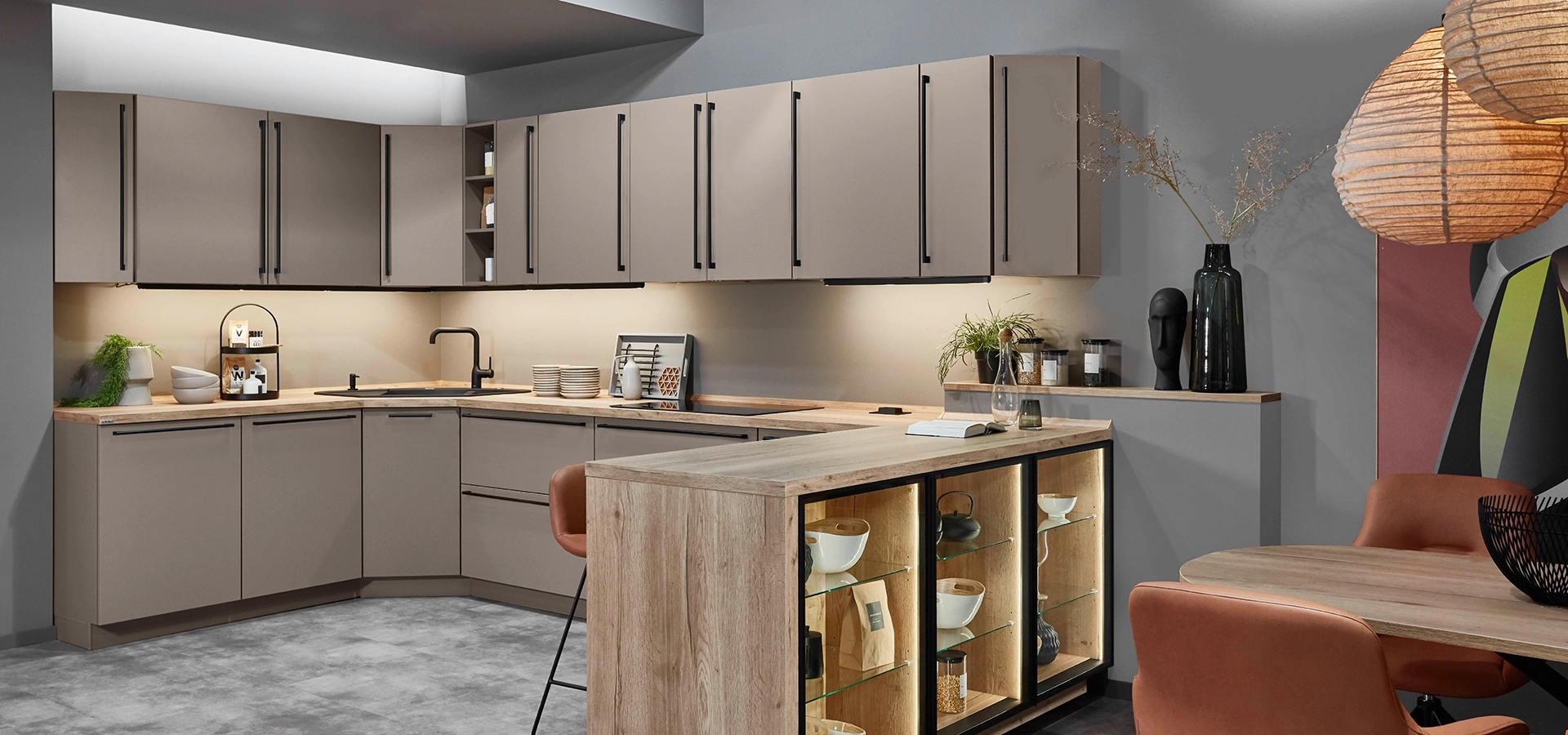 Küche der Art Wohnküche in U-Form mit Vitrinen. Die Front ist hellbraun und die Relinggriffe schwarz. Küche der Art Wohnküche in U-Form mit Vitrinen. Die Front ist hellbraun und die Relinggriffe schwarz.