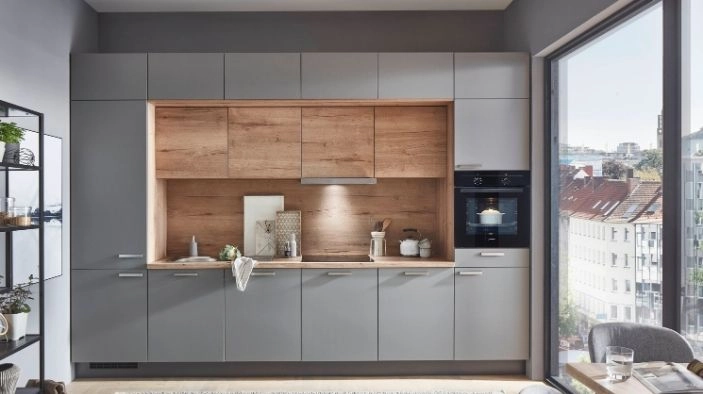 Küchenzeile in Grau mit integriertem Holz‑Nischenbereich – Holzrückwand und Arbeitsplatte, zentral Spüle und Kochfeld, rechts Einbaubackofen. Großes Fenster mit urbanem Ausblick. Küchenzeile in Grau mit integriertem Holz‑Nischenbereich – Holzrückwand und Arbeitsplatte, zentral Spüle und Kochfeld, rechts Einbaubackofen. Großes Fenster mit urbanem Ausblick.