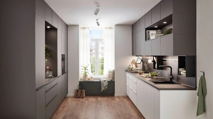 Zweizeilige Küche in schmalem, rechteckigen Raum – dunkle, matte Fronten gegenüber weißer Zeile; Oberschränke mit Nischenregalen, dunkle Rückwand, integrierte Geräte. Fenster mit Sitzbank, viel Tageslicht, Holzoptik‑Boden, moderner Look. Zweizeilige Küche in schmalem, rechteckigen Raum – dunkle, matte Fronten gegenüber weißer Zeile; Oberschränke mit Nischenregalen, dunkle Rückwand, integrierte Geräte. Fenster mit Sitzbank, viel Tageslicht, Holzoptik‑Boden, moderner Look.