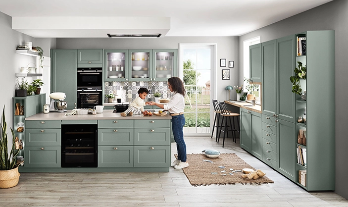 Mutter und Kind, ca. 2 Jahre alt, in einer großen Wohnküche mit schilffarbenen Rahmenfronten. Das Kind sitzt auf der Kochinsel, die Mutter steht daneben. Mutter und Kind, ca. 2 Jahre alt, in einer großen Wohnküche mit schilffarbenen Rahmenfronten. Das Kind sitzt auf der Kochinsel, die Mutter steht daneben.