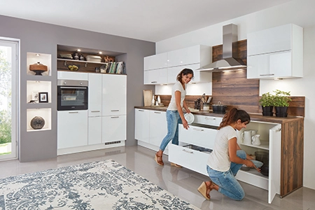 Eine junge Frau ist in zwei Einstellungen in einer weißen Eckküche zu sehen. Einmal öffnet sie einen Unterschrank mit Auszug, ein anderes Mal einen Unterschrank mit einfacher Drehtür. Klassische Küchenplanung. Eine junge Frau ist in zwei Einstellungen in einer weißen Eckküche zu sehen. Einmal öffnet sie einen Unterschrank mit Auszug, ein anderes Mal einen Unterschrank mit einfacher Drehtür. Klassische Küchenplanung.