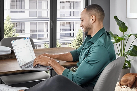 Ein junger Mann im grünen schimmernden Hemd sitzt am Küchentisch und wählt am Laptop ein Küchenstudio aus. Ein junger Mann im grünen schimmernden Hemd sitzt am Küchentisch und wählt am Laptop ein Küchenstudio aus.