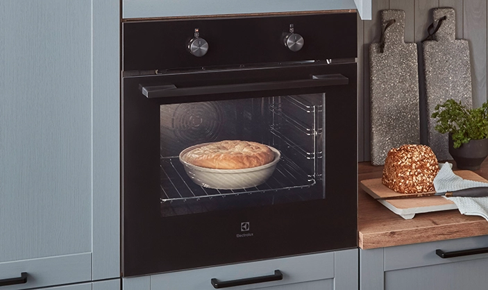 Fokus auf hoch eingebautem Ofen in einer Küche mit blauer Rahmenfront. Im Ofen ist eine Auflaufschale mit Teig. Fokus auf hoch eingebautem Ofen in einer Küche mit blauer Rahmenfront. Im Ofen ist eine Auflaufschale mit Teig.