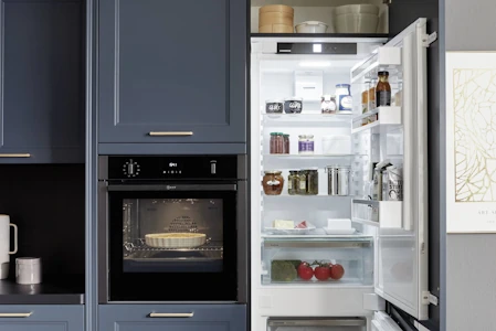 Ein geöffneter Kühlschrank in einer Küche mit einer blauen Landhausfront Ein geöffneter Kühlschrank in einer Küche mit einer blauen Landhausfront