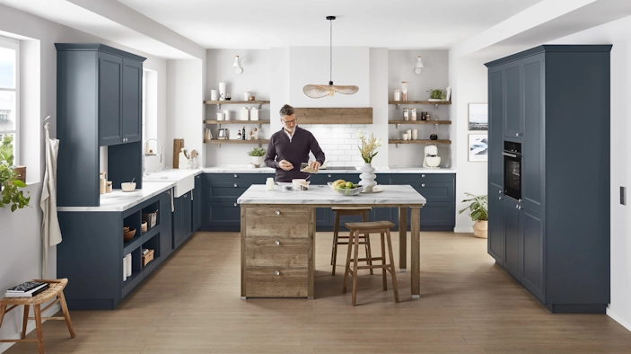 Große Landhausküche mit dunklen Fronten und Holzdetails; ein Mann steht an der Kücheninsel und bereitet etwas zu. Große Landhausküche mit dunklen Fronten und Holzdetails; ein Mann steht an der Kücheninsel und bereitet etwas zu.