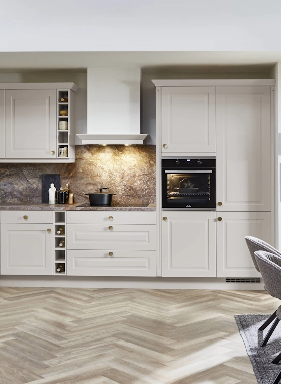 Helle Landhausküche mit Rahmenfronten, Marmoroptik-Rückwand und integrierten Weinregalen, vor einem Parkettboden in Fischgrätmuster. Helle Landhausküche mit Rahmenfronten, Marmoroptik-Rückwand und integrierten Weinregalen, vor einem Parkettboden in Fischgrätmuster.