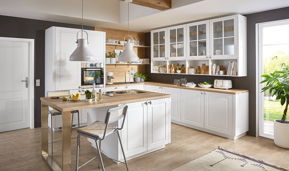 Wir sehen eine offene mediterrane Küche mit weißen Kassettenfronten. Sie besteht aus einer Eckküche sowie einer Kochinsel. Wir sehen eine offene mediterrane Küche mit weißen Kassettenfronten. Sie besteht aus einer Eckküche sowie einer Kochinsel.