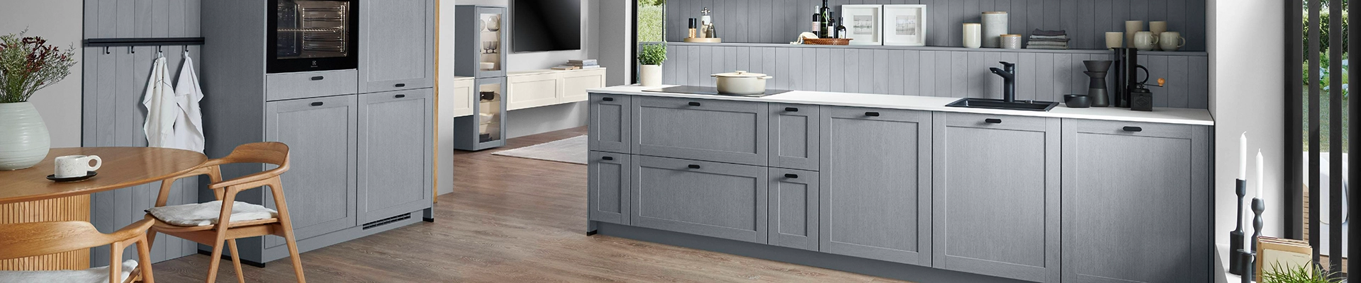 Moderne graue Landhausküche mit Rahmenfronten, weißer Arbeitsplatte, schwarzer Spüle und integriertem Backofen; daneben Essbereich mit Holztisch und Stühlen. Moderne graue Landhausküche mit Rahmenfronten, weißer Arbeitsplatte, schwarzer Spüle und integriertem Backofen; daneben Essbereich mit Holztisch und Stühlen.