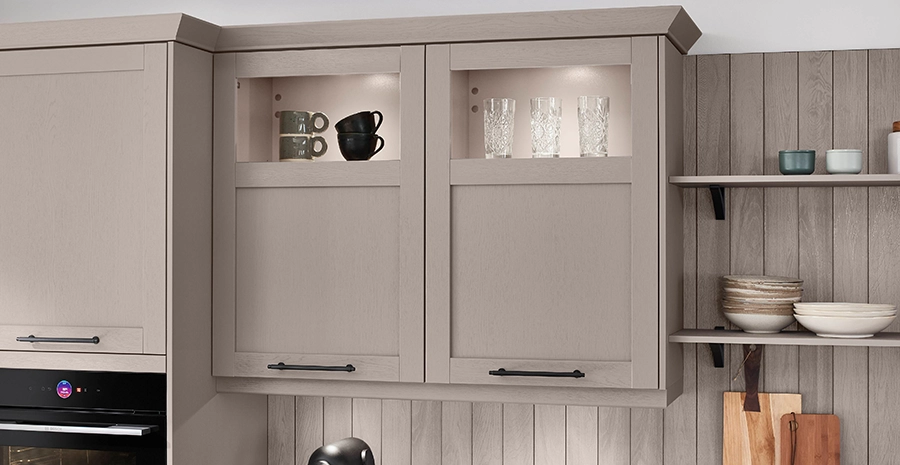 Helle Landhausküche mit grauen Rahmenfronten, gläsernen Oberschrank-Nischen, dunkler Stein-Arbeitsplatte und offenen Regalen mit Geschirr und Holzbrett. Helle Landhausküche mit grauen Rahmenfronten, gläsernen Oberschrank-Nischen, dunkler Stein-Arbeitsplatte und offenen Regalen mit Geschirr und Holzbrett.