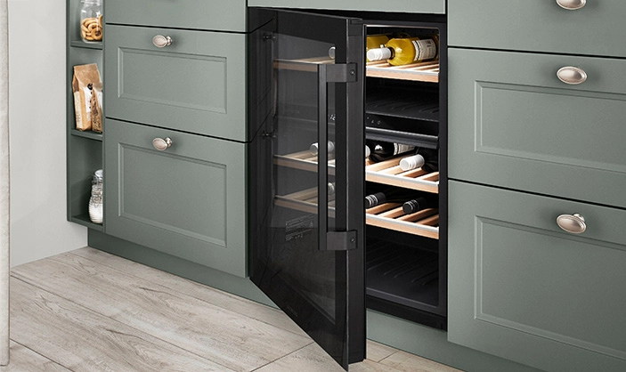 Ausschnitt einer Küche mit salbeigrüner Rahmenfront und integriertem geöffneten Weinkühlschrank. Ausschnitt einer Küche mit salbeigrüner Rahmenfront und integriertem geöffneten Weinkühlschrank.