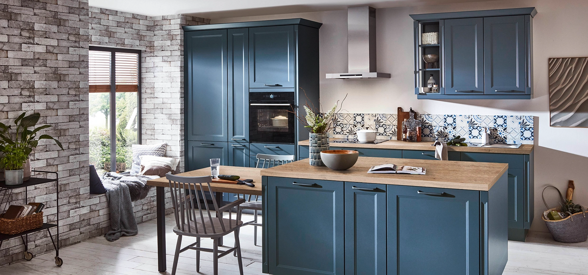 Mediterrane Küche mit blauen Landhausfronten, warmen Holzarbeitsplatten und dekorativer gemusterter Rückwand, ergänzt durch einen zentralen Küchenblock und Essbereich. Mediterrane Küche mit blauen Landhausfronten, warmen Holzarbeitsplatten und dekorativer gemusterter Rückwand, ergänzt durch einen zentralen Küchenblock und Essbereich.