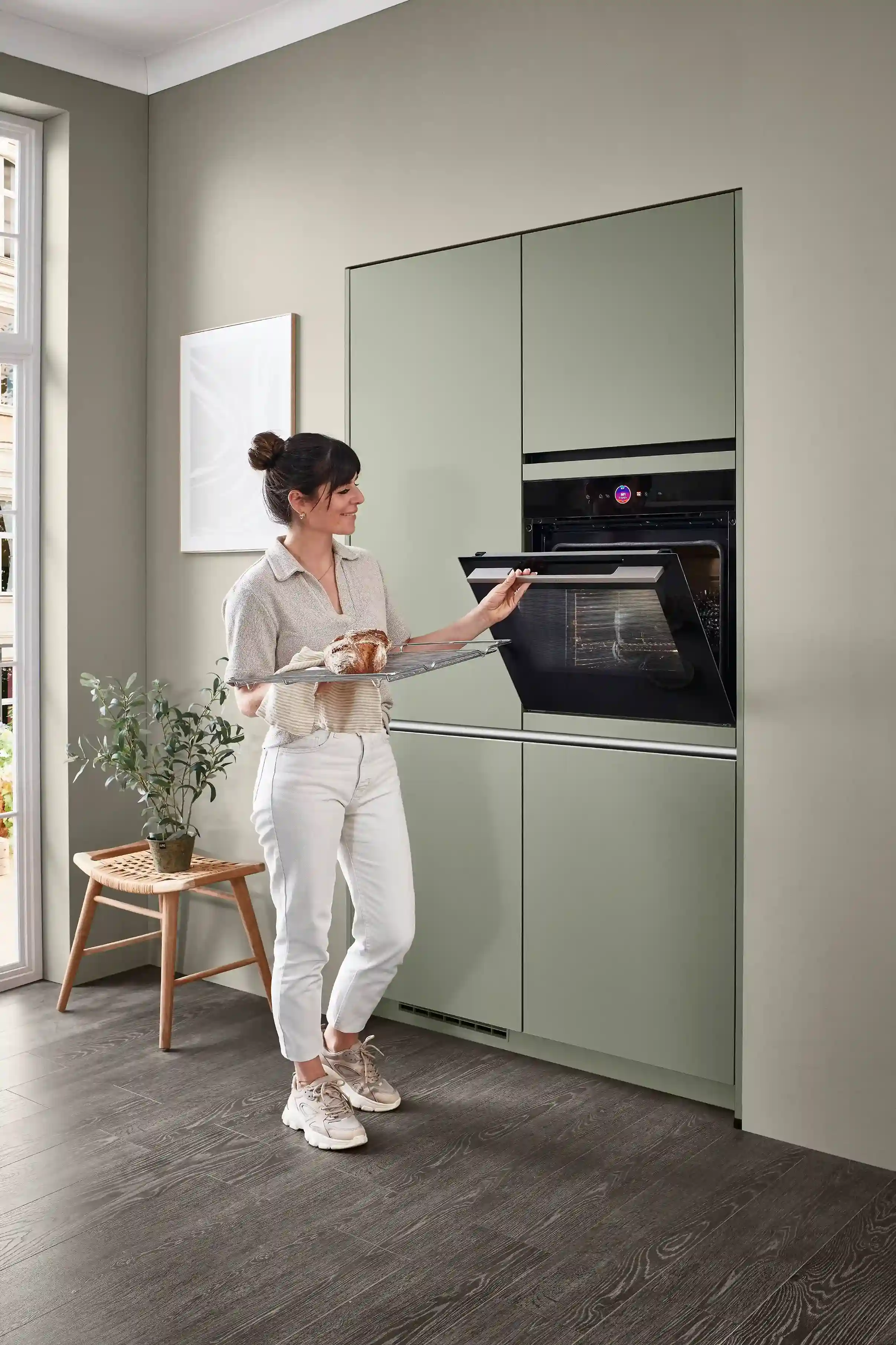 Frau schiebt Backwaren in den Ofen einer modernen Küche, als Beispiel für praktische Ausstattung und modernes Küchendesign Frau schiebt Backwaren in den Ofen einer modernen Küche, als Beispiel für praktische Ausstattung und modernes Küchendesign