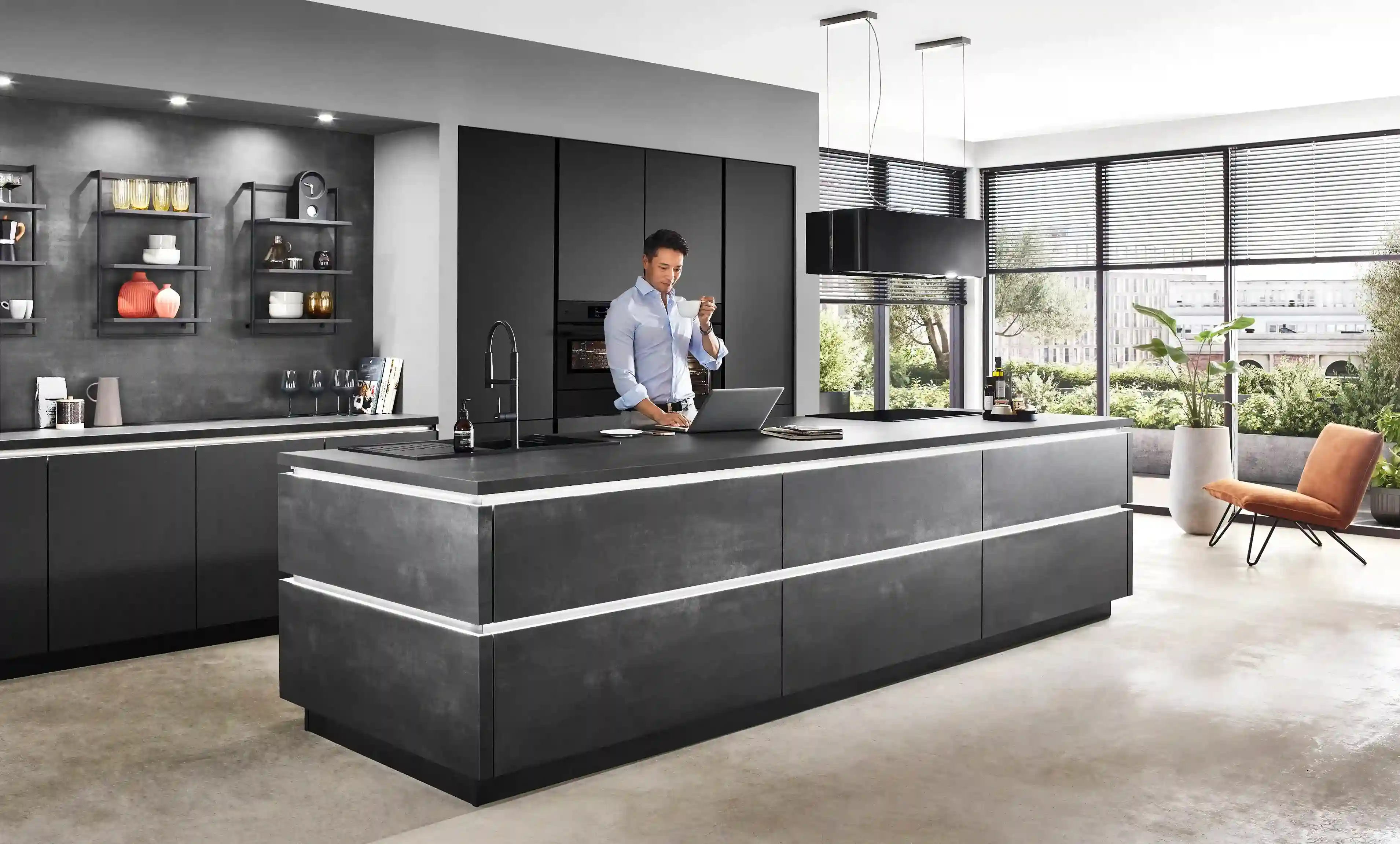 Mann arbeitet am Laptop und trinkt Kaffee in einer modernen dunklen Inselküche mit klaren Linien, Beispiel für edle Optik und modernes Küchendesign Mann arbeitet am Laptop und trinkt Kaffee in einer modernen dunklen Inselküche mit klaren Linien, Beispiel für edle Optik und modernes Küchendesign