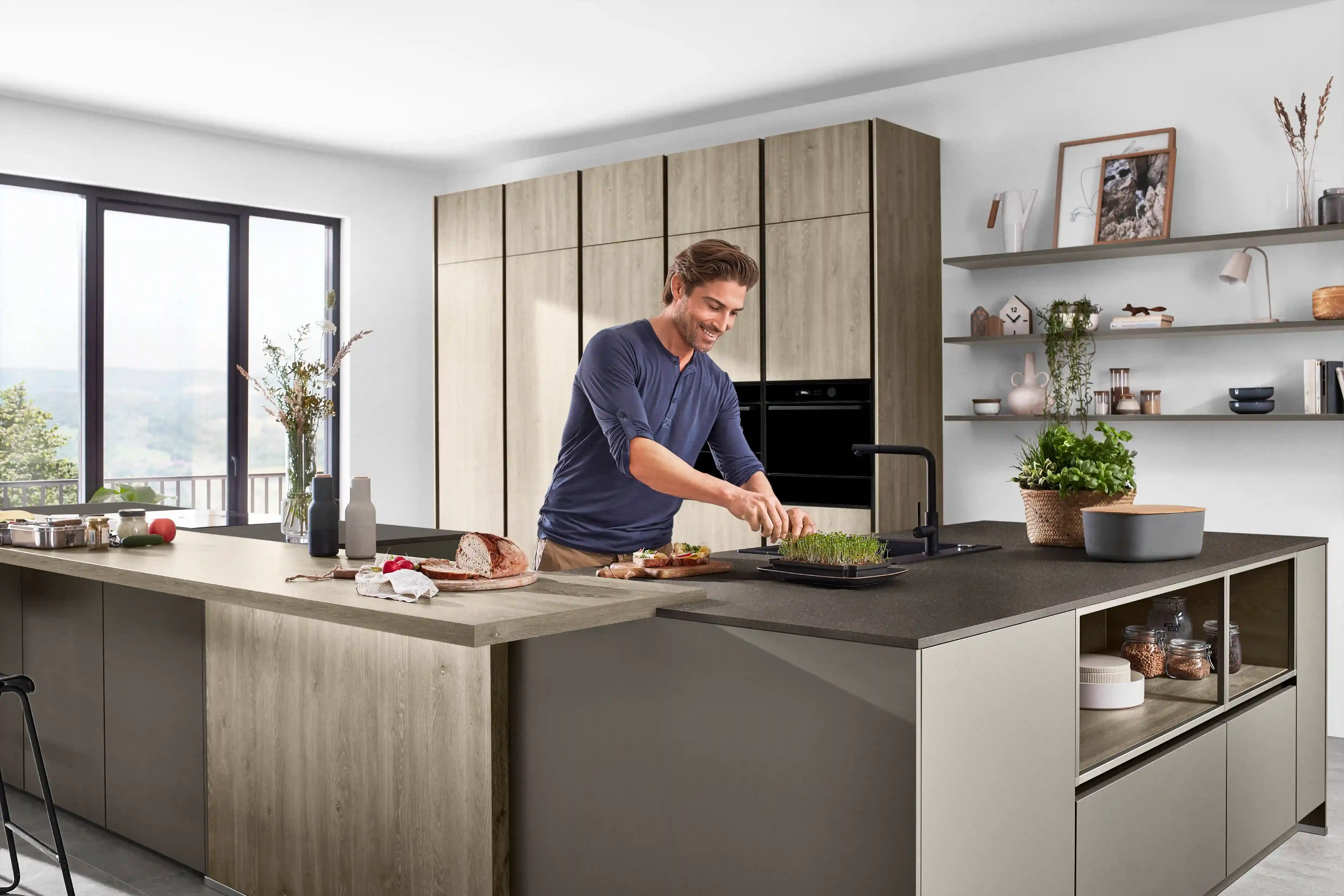 Mann bereitet in einer modernen Inselküche mit Holzakzenten eine Speise zu, als Beispiel für die individuelle Küchenplanung Mann bereitet in einer modernen Inselküche mit Holzakzenten eine Speise zu, als Beispiel für die individuelle Küchenplanung