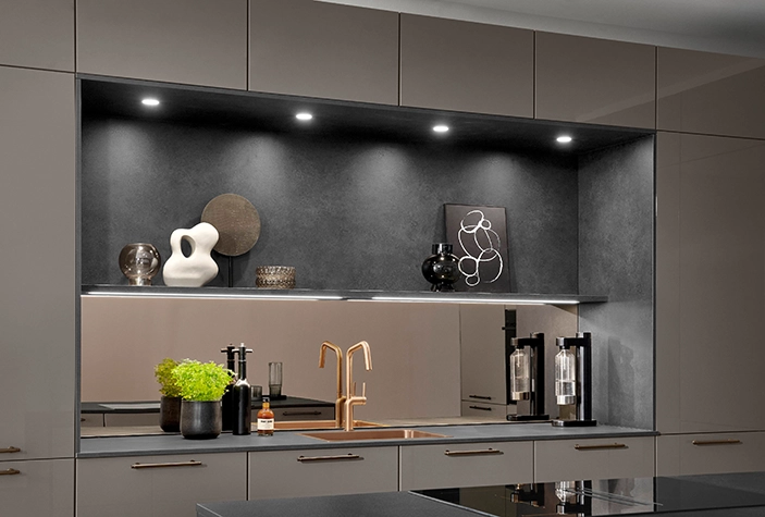 Ausschnitt einer Küche in einem Erdton mit beleuchteter Nische. Die Nische hat eine kontrastreiche schwarze Verkleidung. Ausschnitt einer Küche in einem Erdton mit beleuchteter Nische. Die Nische hat eine kontrastreiche schwarze Verkleidung.