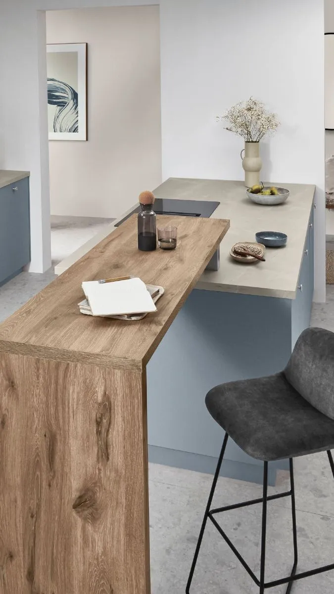 Moderne Küche mit hellblauen Unterschränken, heller Arbeitsplatte und einer Holz-Theke mit Barhockern. Moderne Küche mit hellblauen Unterschränken, heller Arbeitsplatte und einer Holz-Theke mit Barhockern.