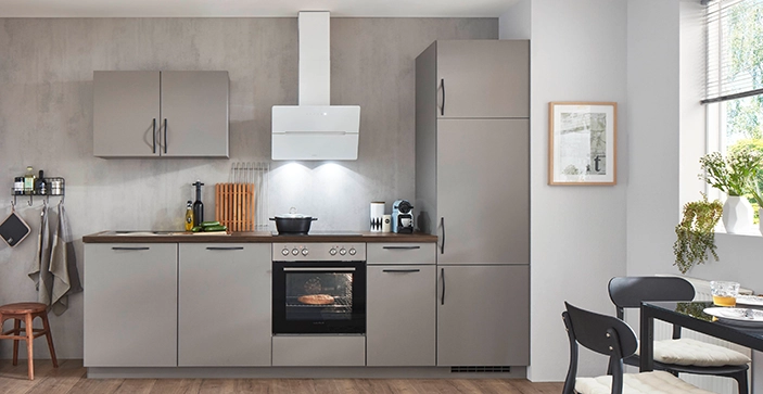 Hellgraue Pantryküche mit weißer Dunsthaube, Wandschrank und Hochschrank. Rechts sehen wir einen Esstisch und zwei Stühle. Hellgraue Pantryküche mit weißer Dunsthaube, Wandschrank und Hochschrank. Rechts sehen wir einen Esstisch und zwei Stühle.